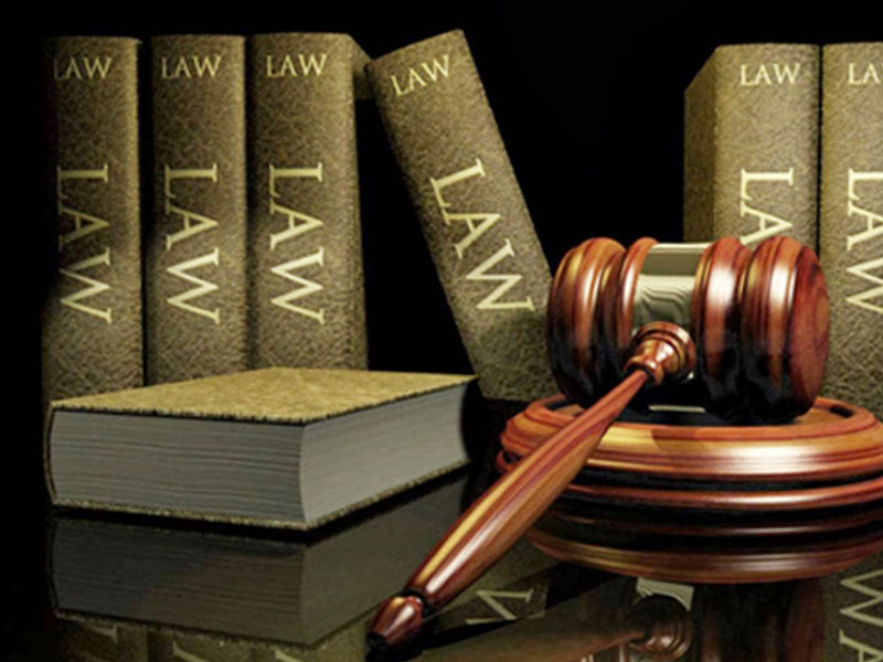 A judge's gavel rests on its block beside several law books, all labeled "LAW," against a dark background.